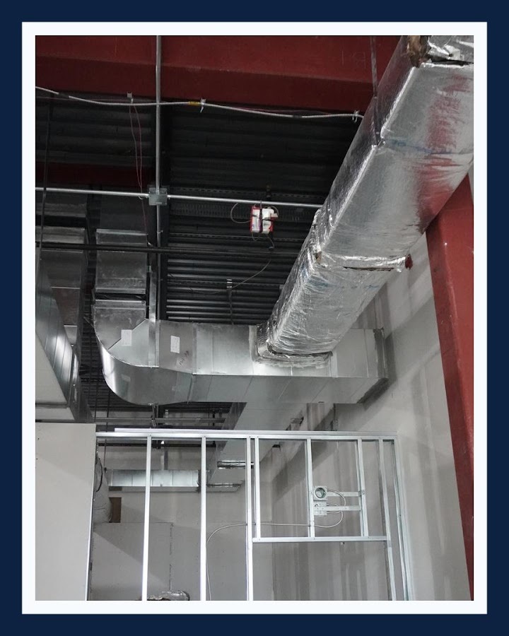 Fabricated rectangular sheet metal ductwork with elbows and transitions installed under an open commercial ceiling.
